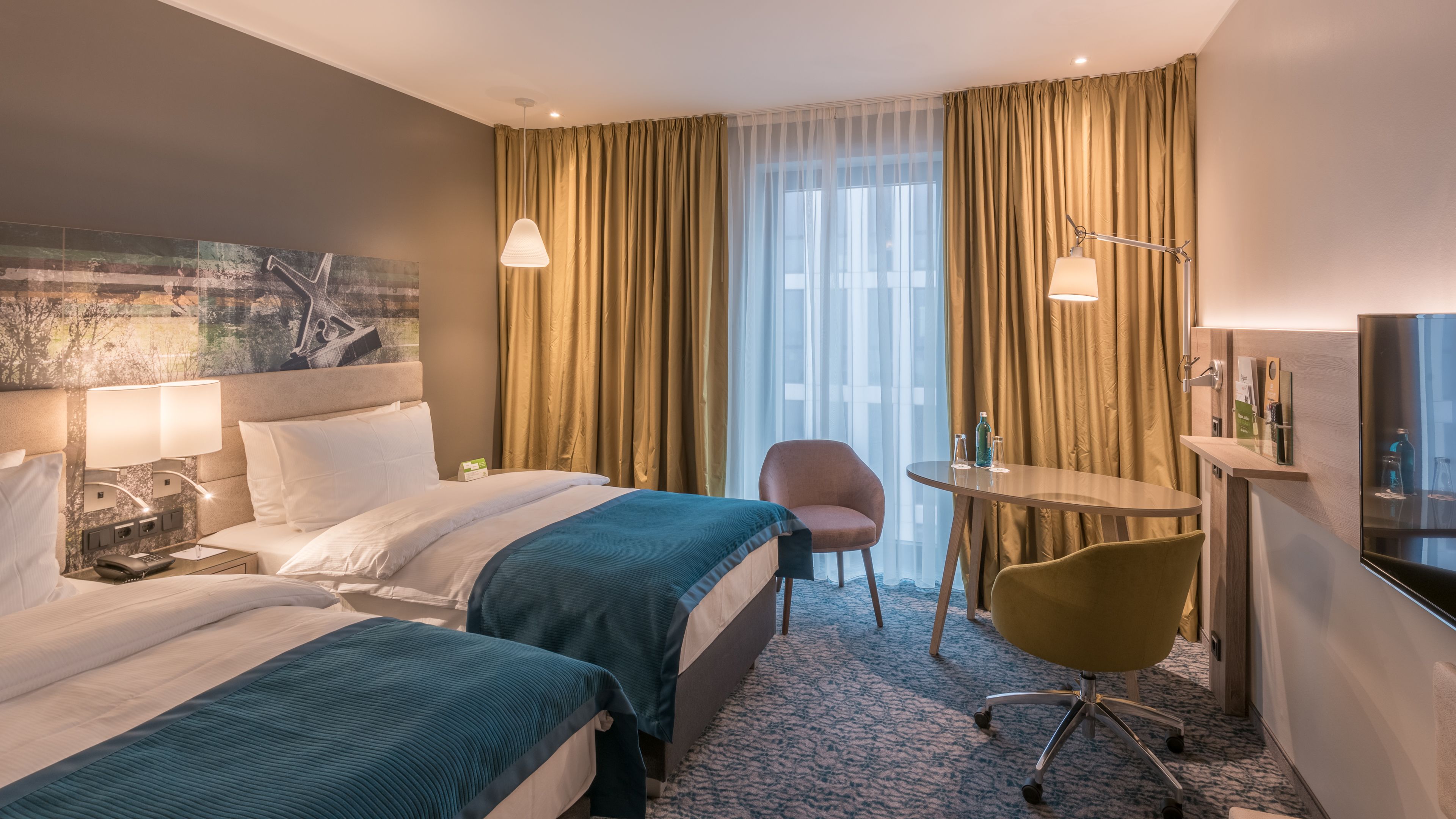 A hotel room with two beds, a desk, a chair, a TV, and a painting on the wall.