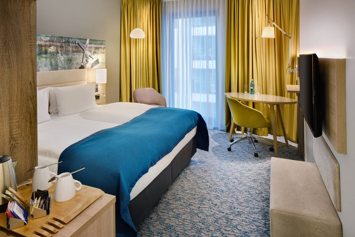 Habitación de hotel con una cama grande, un escritorio con silla, televisor y ventana con cortinas.
