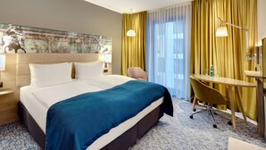 A hotel room with a large bed, a desk with a chair, a lamp, and a painting on the wall.