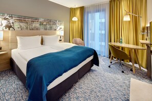 Habitación de hotel con una cama grande, un escritorio con una silla, una lámpara y un cuadro en la pared.