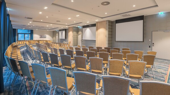 Une salle de conférence avec des rangées de chaises, un grand écran et un projecteur.