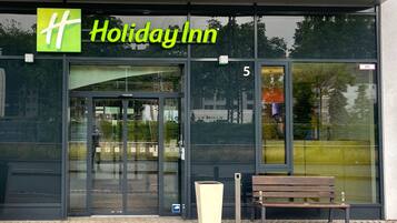 Holiday Inn -hotellin ulkonäkö: lasinen sisäänkäynti, ulkona oleva penkki ja esteetön näkymä ympäröivään alueeseen.