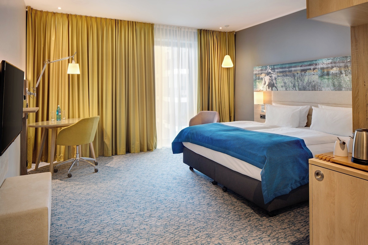 Una habitación de hotel con cama, escritorio, silla y un cuadro en la pared.