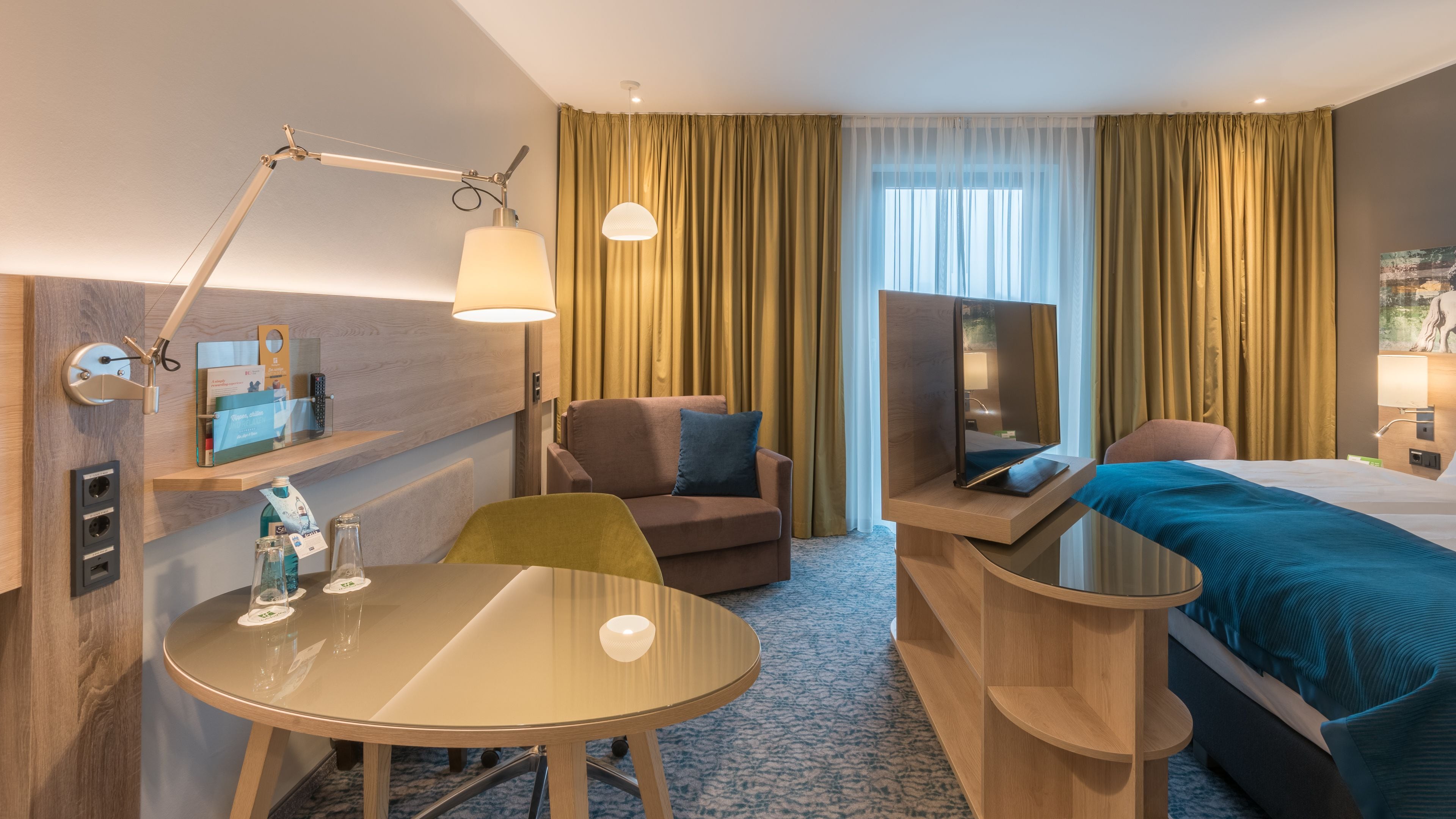 Una habitación de hotel con cama, escritorio con silla, sofá, televisor y lámpara.