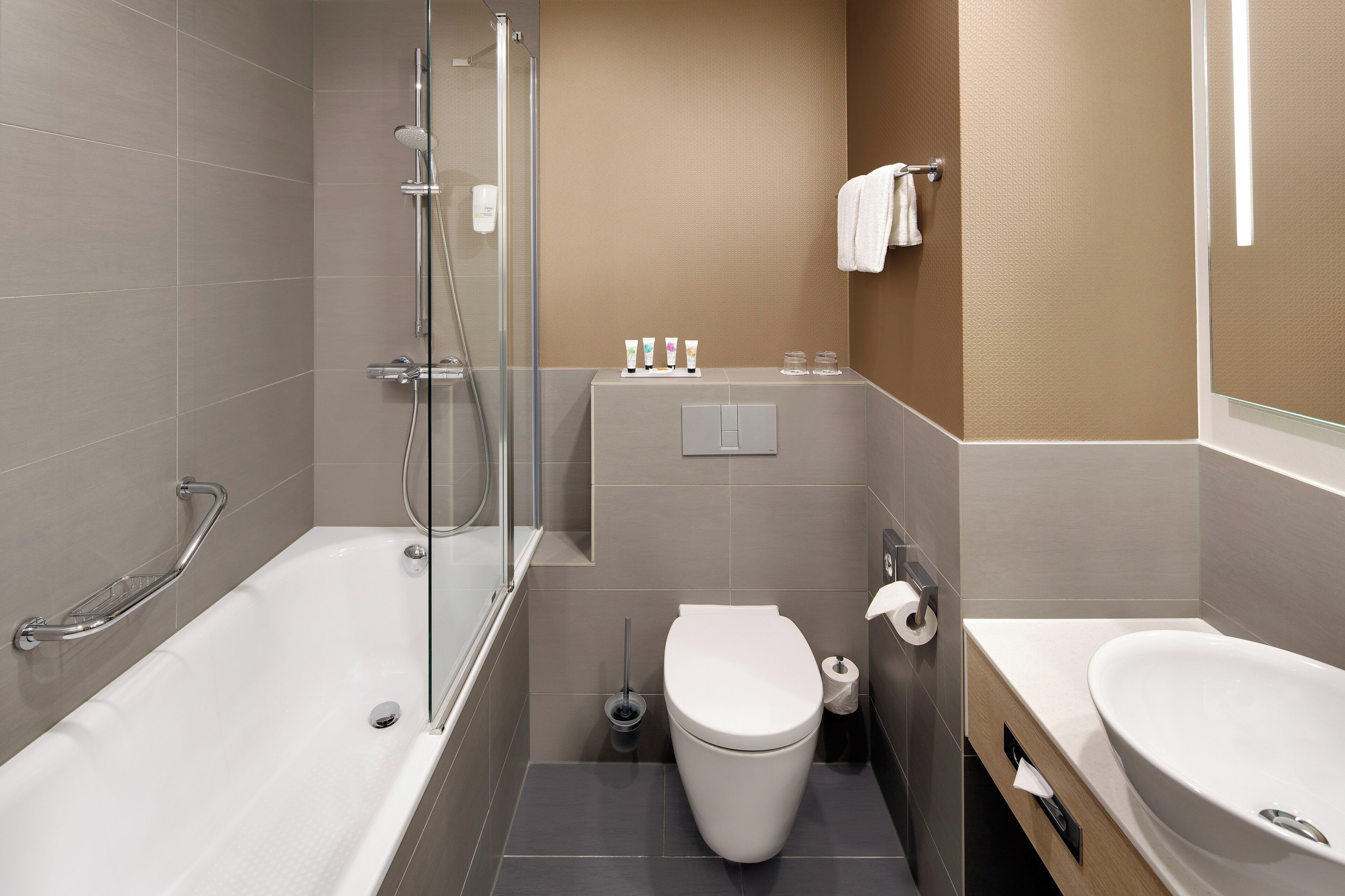 A modern bathroom with a bathtub, toilet, and sink, featuring a glass shower enclosure and a towel rack.