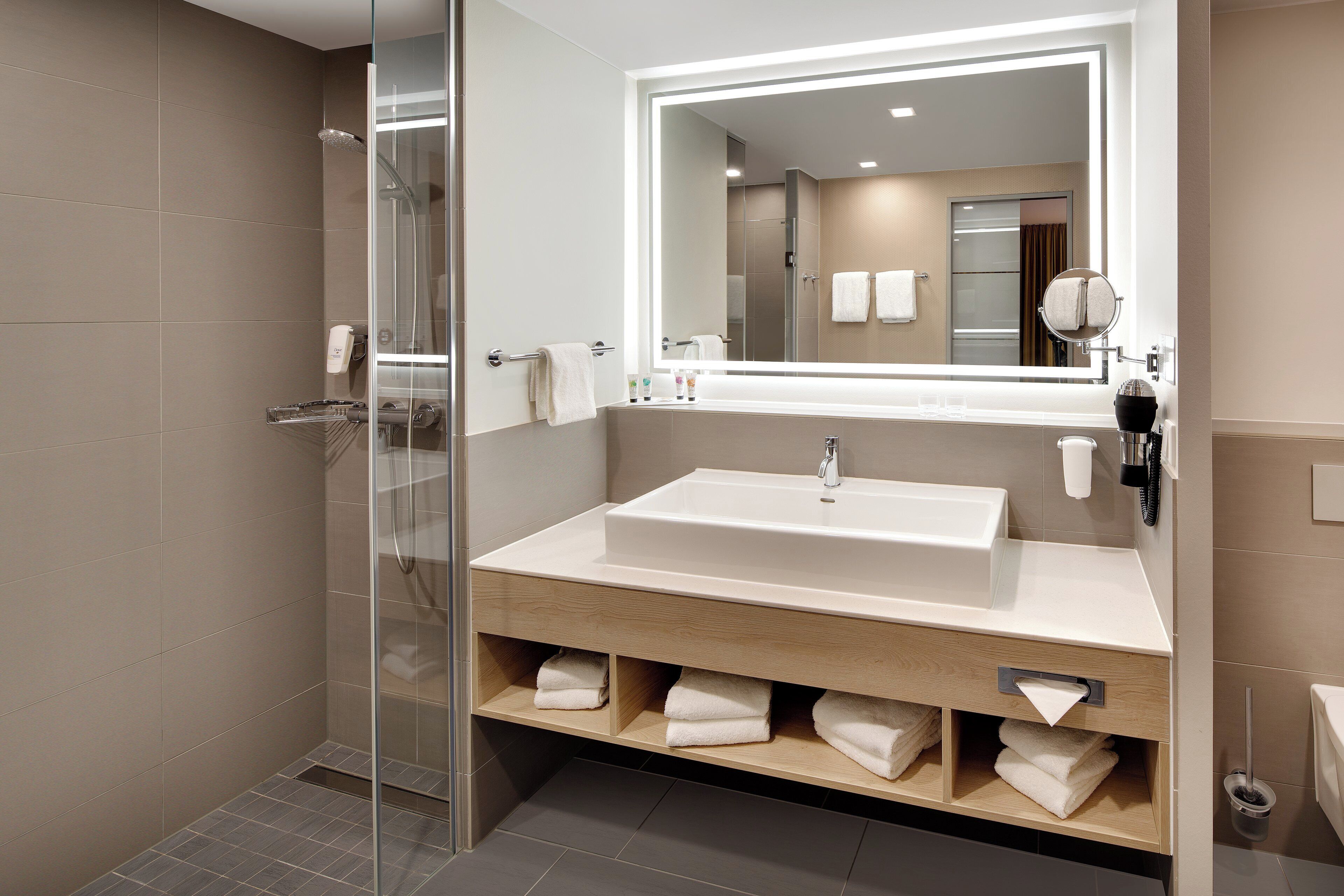 A modern bathroom with a glass shower enclosure, a large mirror, a sink with a vanity, and neatly folded towels.