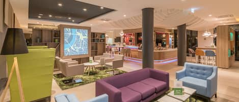 A modern hotel lobby with seating areas, a bar, and a large digital map display.