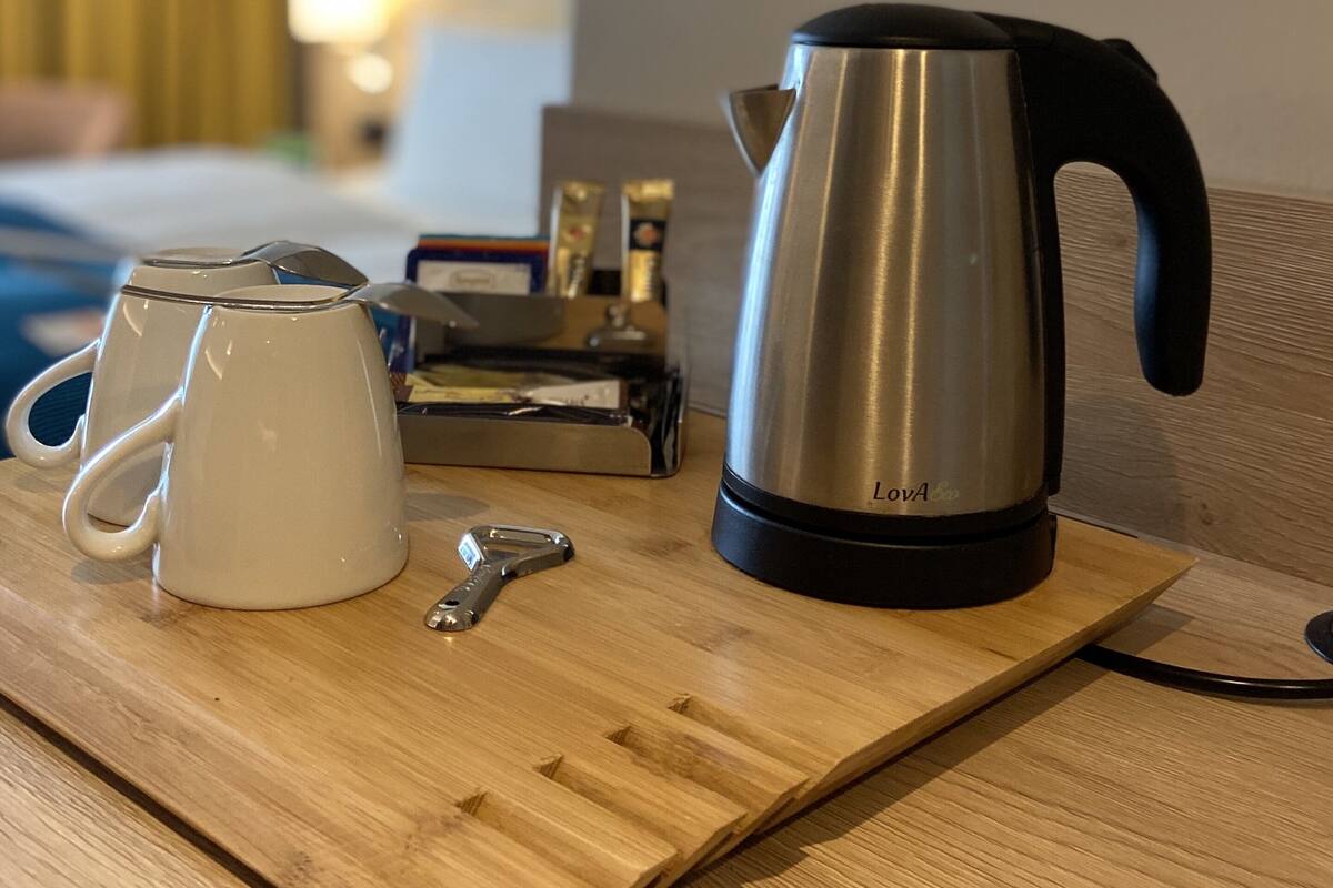 Una bandeja de madera con una tetera, una cafetera y una taza sobre una mesa.