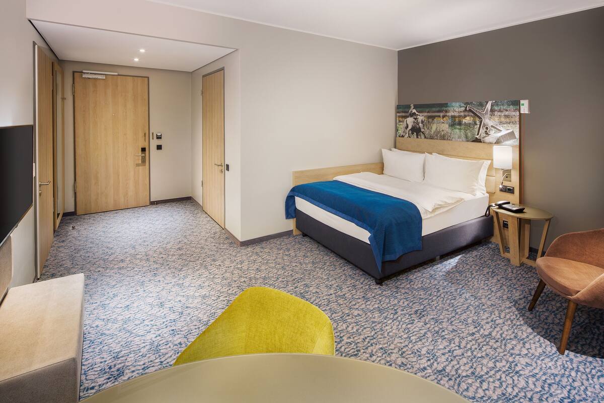 Una habitación de hotel con cama, escritorio, silla y un cuadro en la pared.