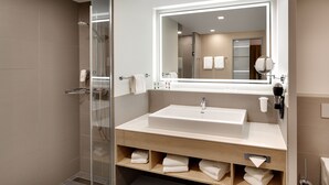 A modern bathroom with a glass-enclosed shower, a large mirror, and a wooden vanity with multiple towel drawers.