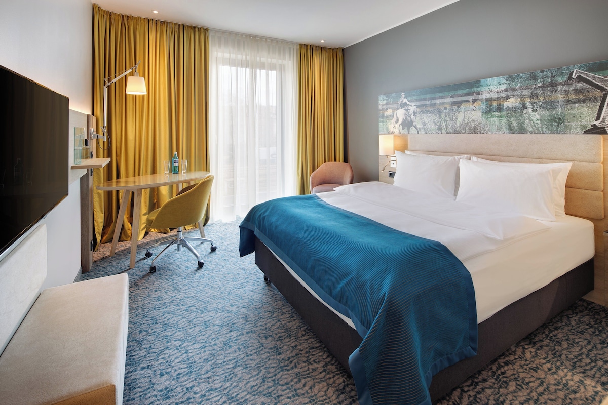 Habitación de hotel con cama, escritorio, silla y televisión.