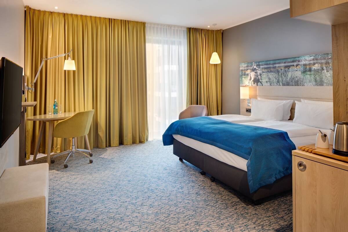 Una habitación de hotel con una cama, un escritorio, una silla, un televisor y un cuadro en la pared.