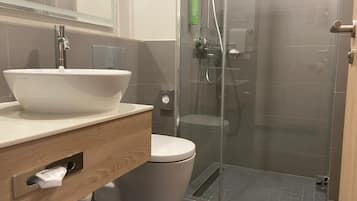 A modern bathroom with a large white basin, a toilet, and a glass-enclosed shower area.