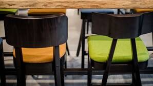 Un espace de salle à manger moderne avec une longue table en bois, des chaises noires dotées de coussins verts et des suspensions lumineuses orange.