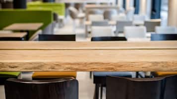 Un comedor moderno con una mesa de madera larga, sillas negras con cojines verdes y lámparas colgantes naranjas.