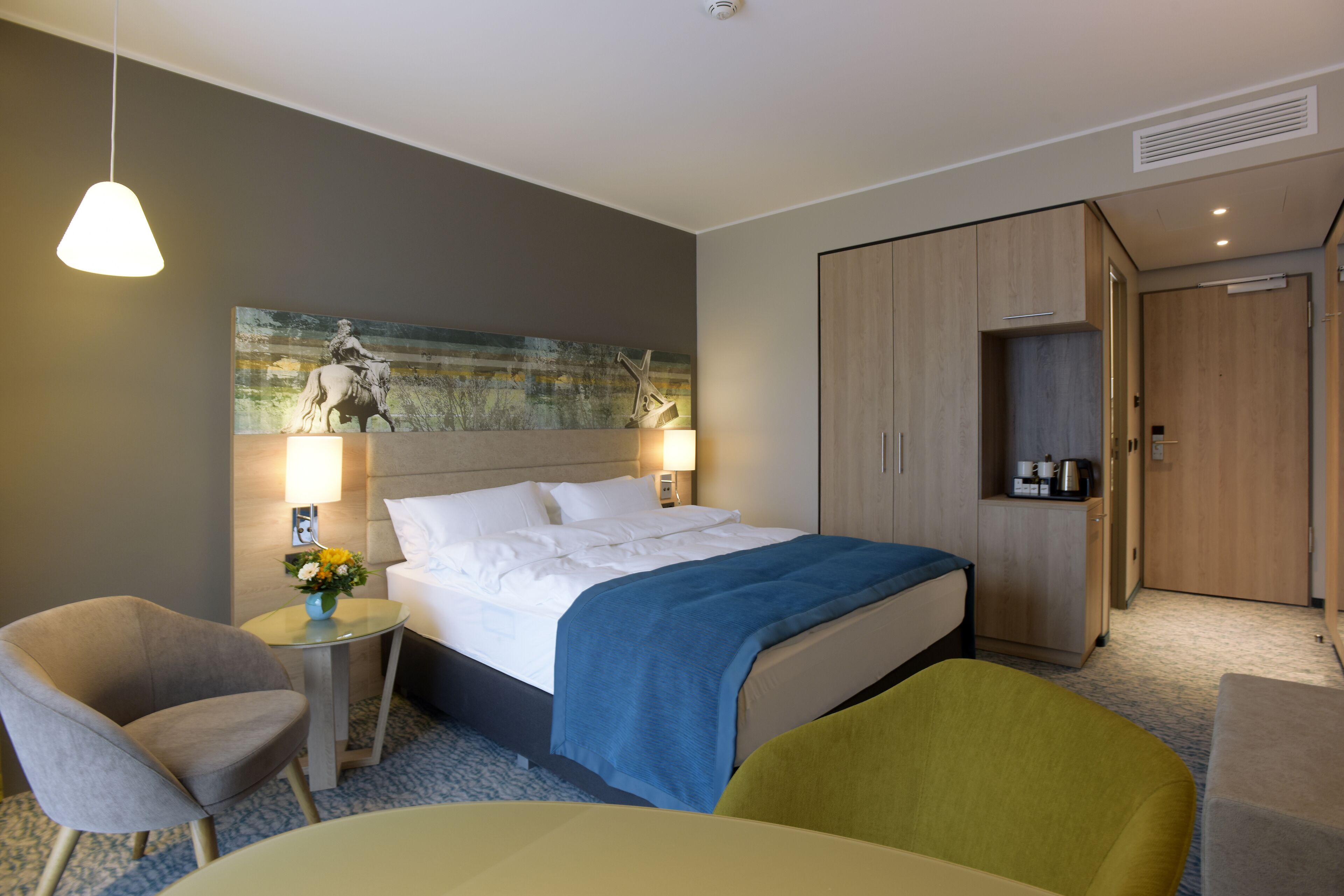 A hotel room with a bed, bedside tables, a chair, a desk, and a wardrobe.