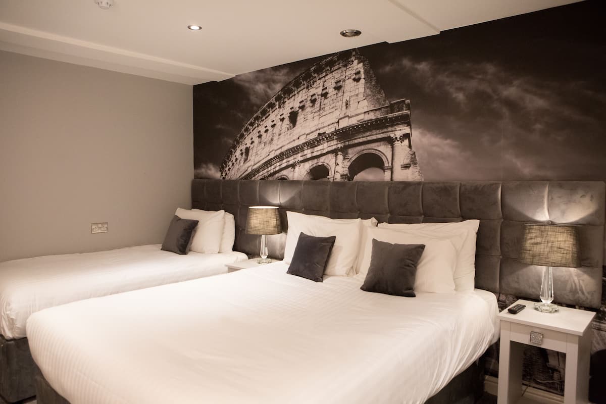 Ein Hotelzimmer mit zwei Betten, einem großen Wandbild des Kolosseums und einem modernen Design.