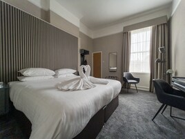 Habitación de hotel con una cama grande, un escritorio, una silla, un espejo y una ventana con cortinas.