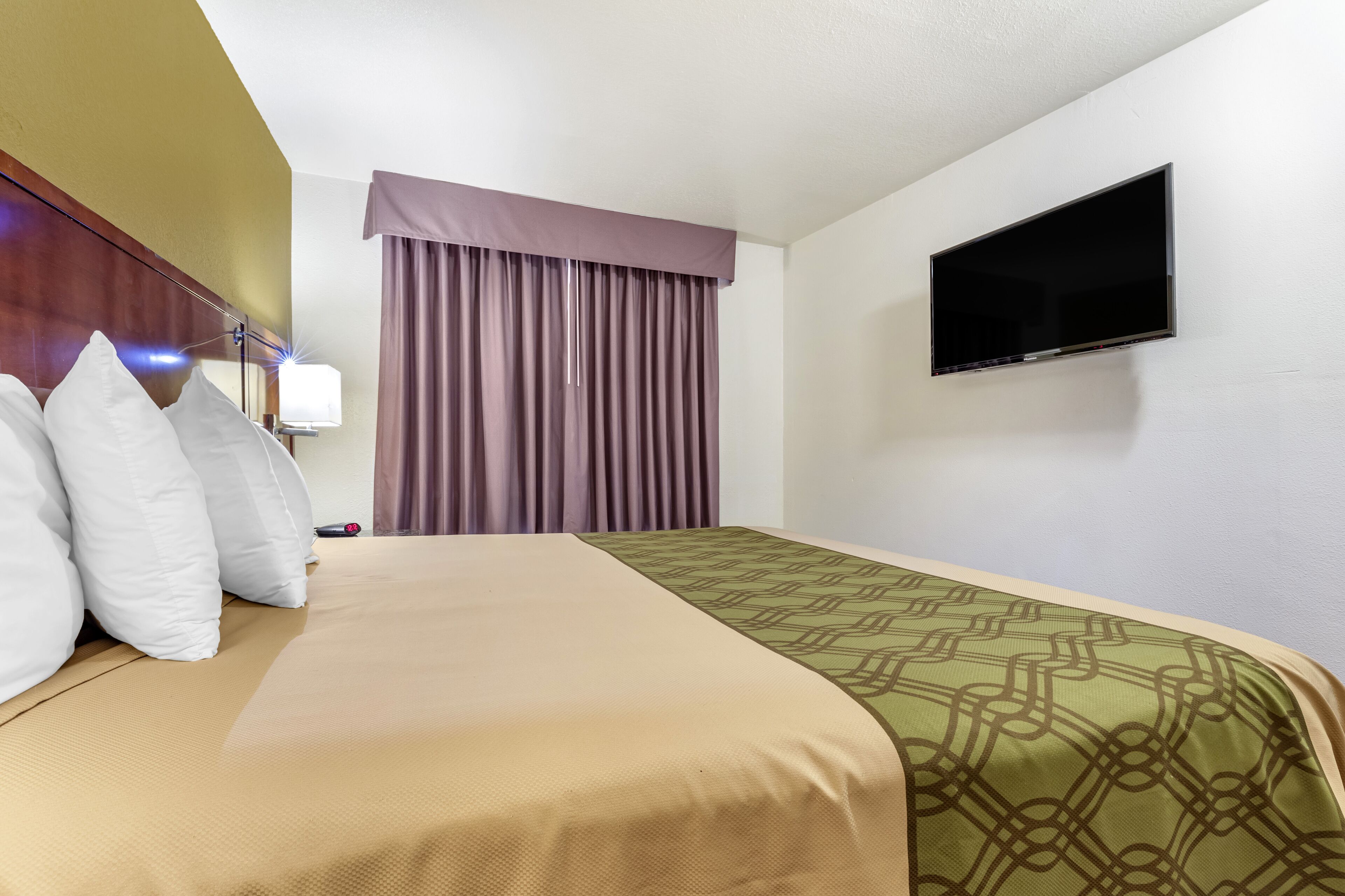 Una camera d'albergo con un letto, una televisione e una finestra con tende.