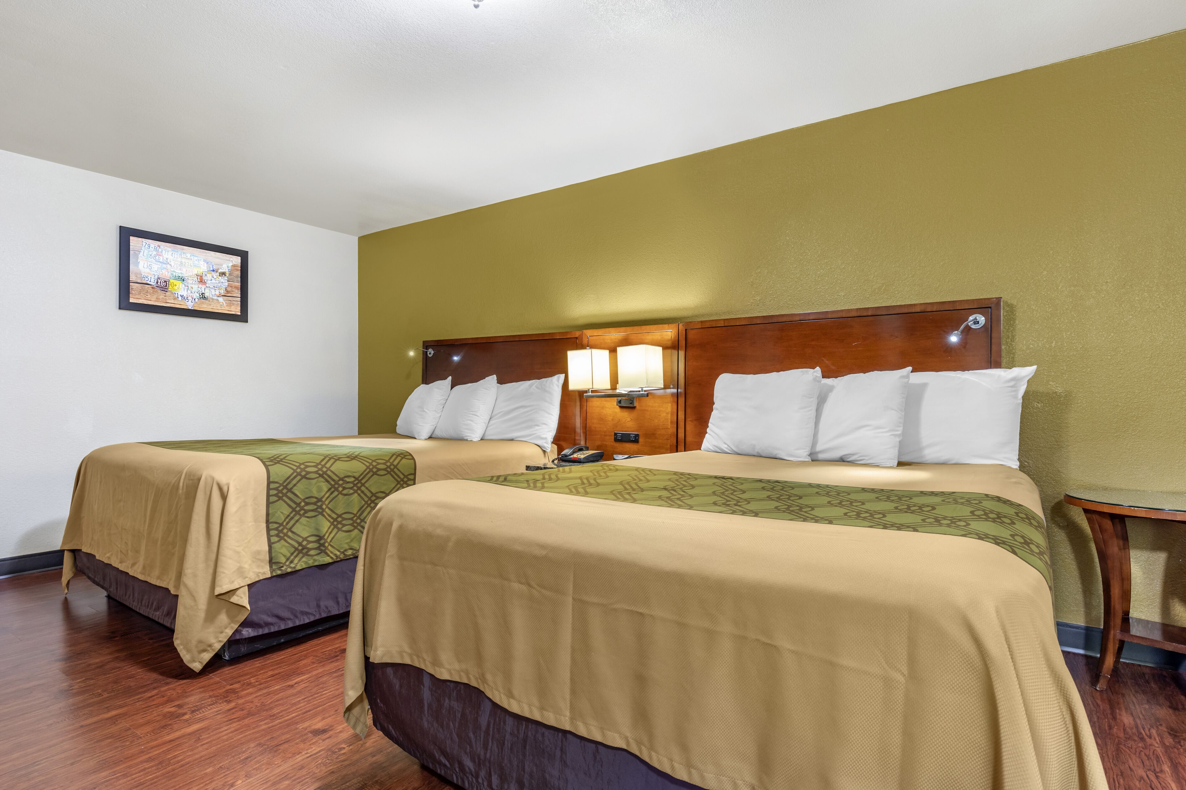 A hotel room with two beds, wooden headboards, and a nightstand with a lamp.