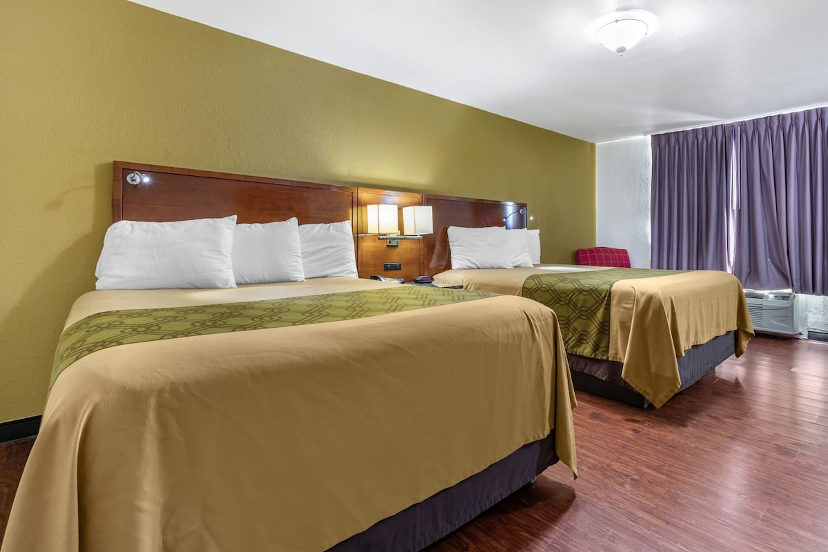 Ett hotellrum med två sängar, trägavlar och ett stort fönster med gardiner.