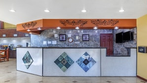 A reception area with a marble counter, framed artwork, a clock, and a TV mounted on the wall. - Rose City Inn & Suites (Tyler)