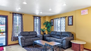 A living area with two grey sofas, a wooden coffee table, and a small round table. - Rose City Inn & Suites (Tyler)