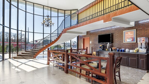 A spacious lobby with a high ceiling, a staircase leading to an upper level, and a kitchen area with a large TV. - Rose City Inn & Suites (Tyler)