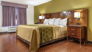 A hotel room with a bed, bedside tables, a lamp, and a window with curtains. - Rose City Inn & Suites (Tyler)