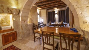 Un comedor rústico con una gran mesa de madera y sillas, paredes de piedra y techo abovedado.
