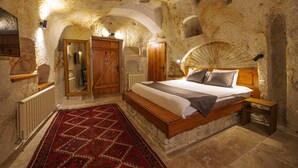 Un dormitorio con pared de piedra, cama de madera y alfombra roja estampada.