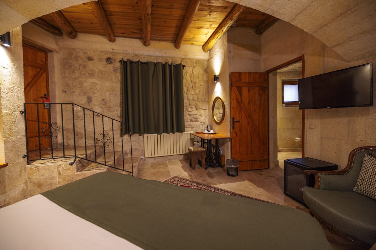 Una habitación rústica con una cama, una silla de madera, un televisor, una máquina de coser y una pared de piedra.