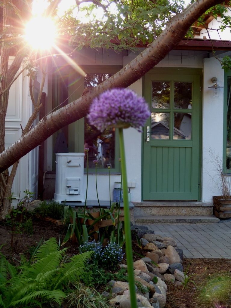 A house with a green door, a white exterior, and a garden with rocks and plants.