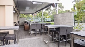 Een terras buiten met meerdere tafels en stoelen, een overdekt zitgedeelte en uitzicht op het omliggende groen.