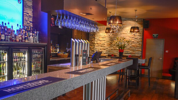 Een bar met een granieten aanrecht, verschillende flesjes drank en een stenen muur met een hangende lamp.