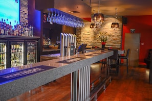 Una zona de bar con encimera de granito, varias botellas de licor y una pared de piedra con una lámpara colgante.