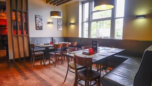 Een restaurant met houten vloeren, een lange tafel met stoelen, een bank en hangende lampen.
