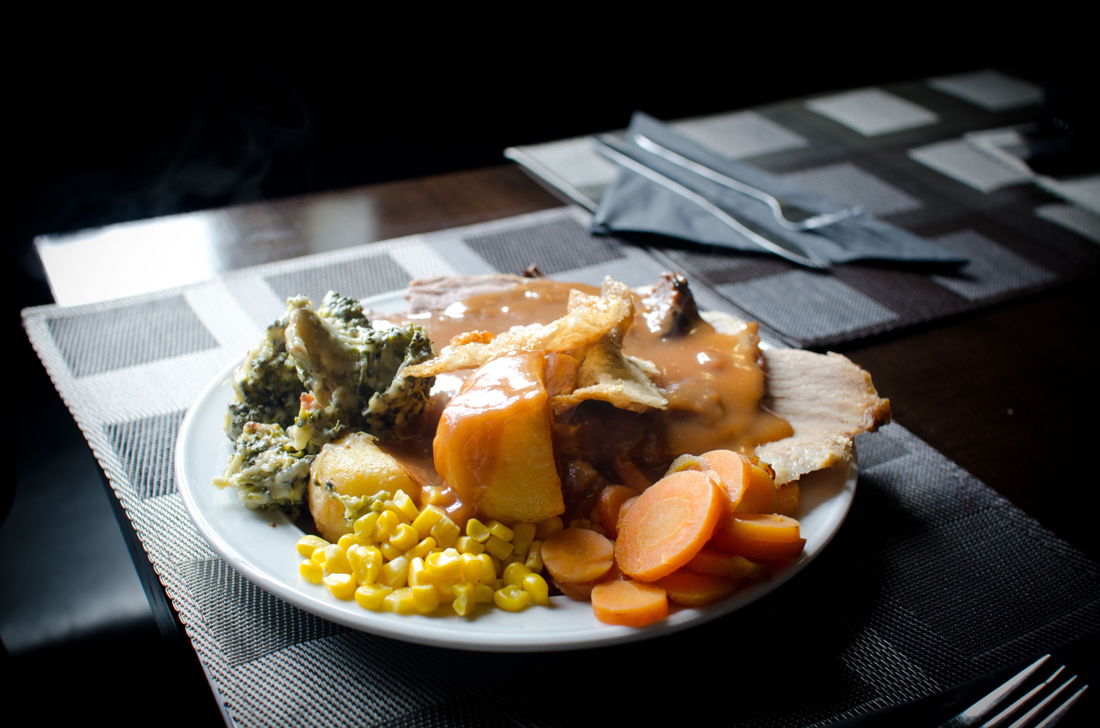 A plate of food with a variety of vegetables and a piece of meat, possibly roast beef, on a table with a placemat.
