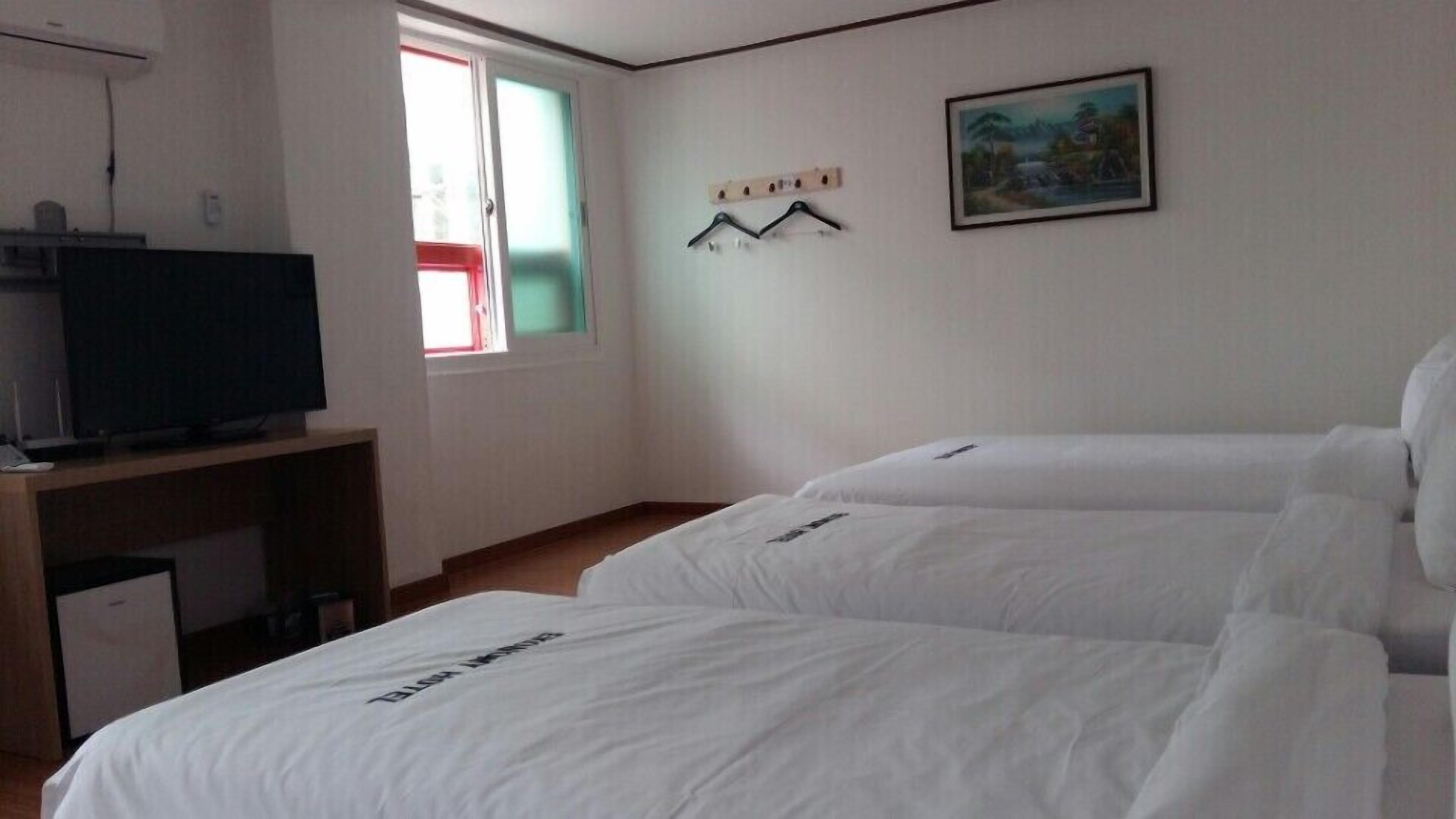 Habitación de hotel con dos camas, un televisor en un escritorio y un cuadro en la pared.