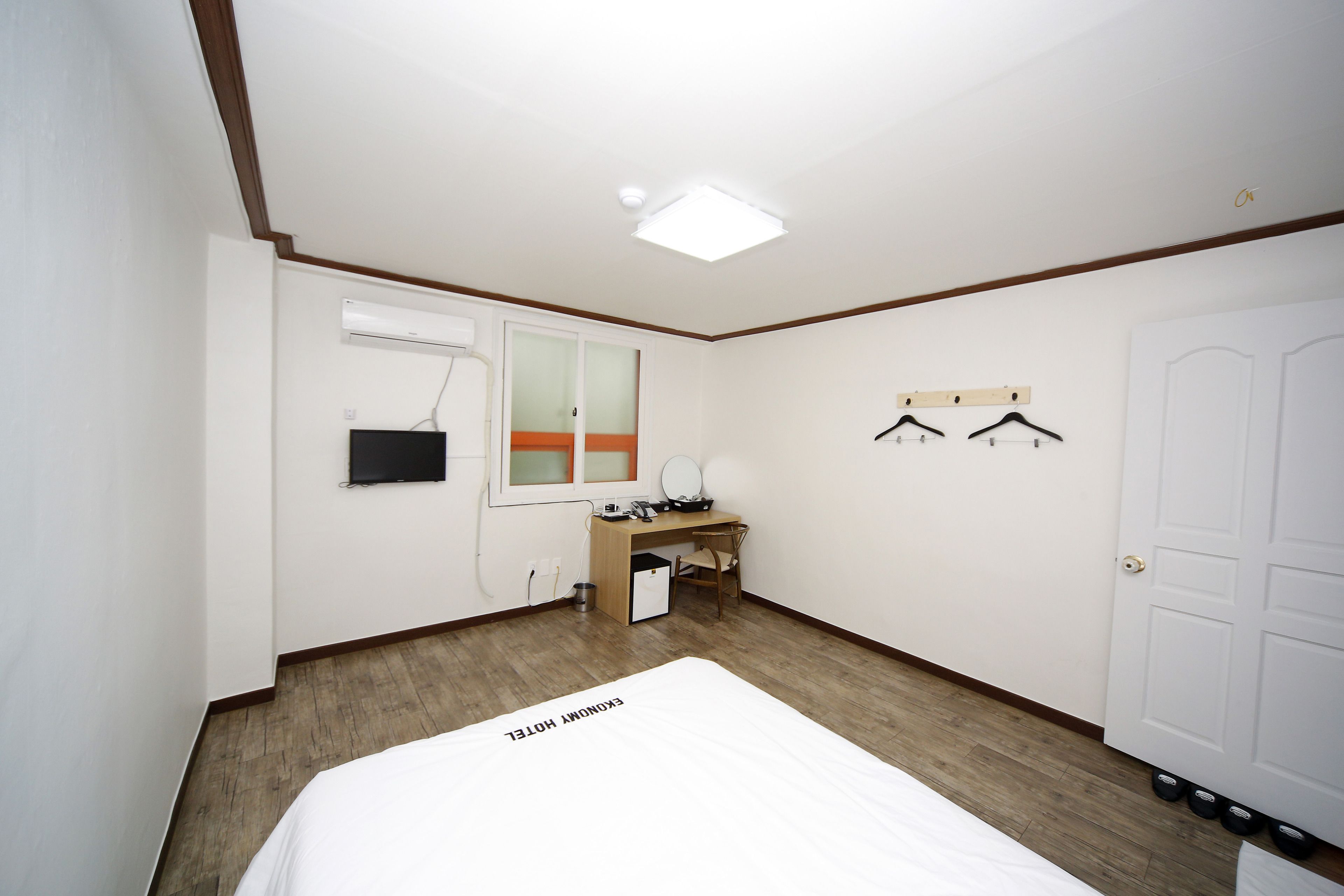 Una habitación de hotel con cama, escritorio, refrigerador pequeño, espejo y un armario para abrigos.