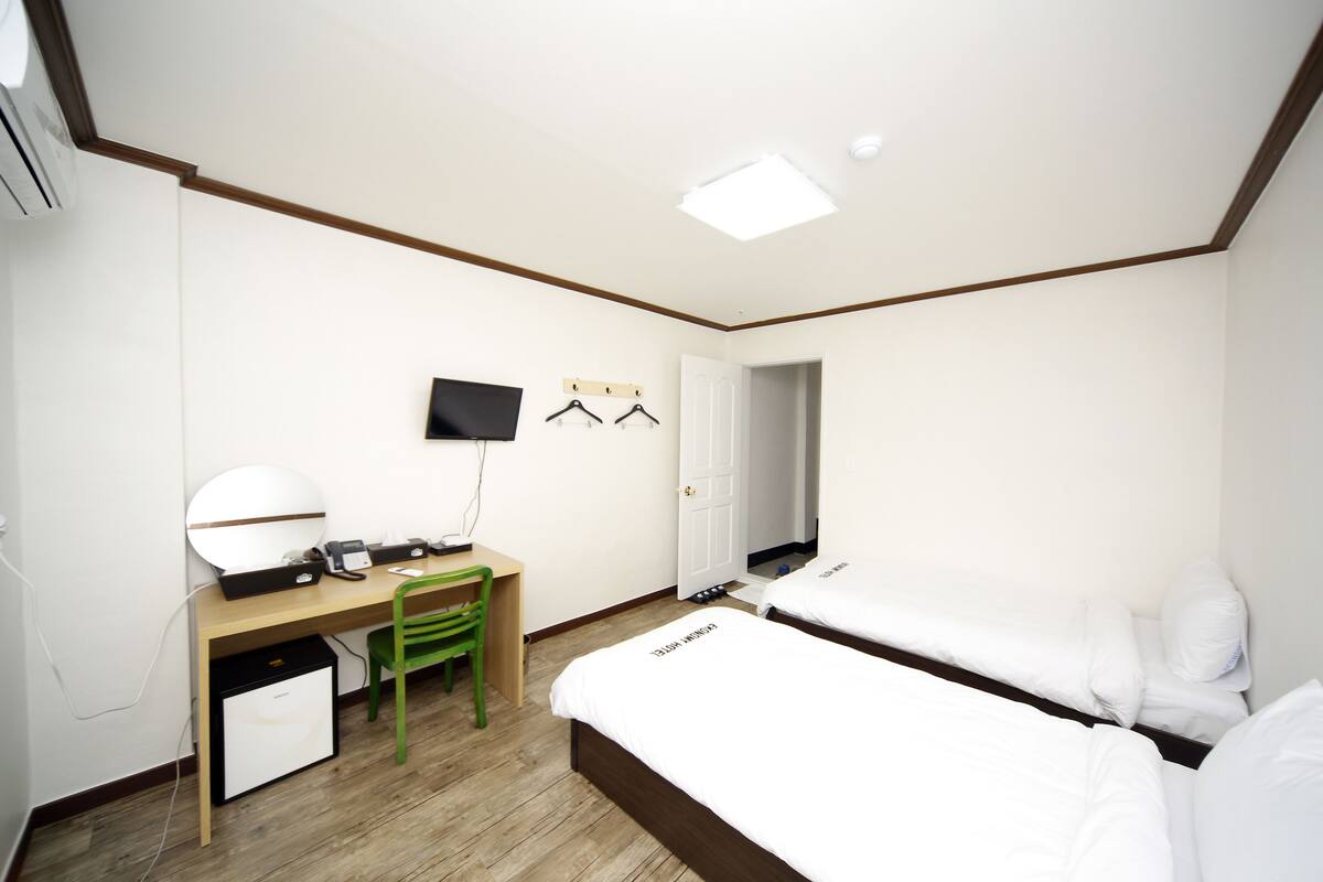 Una habitación de hotel con una cama, un escritorio con silla, un televisor y un perchero.