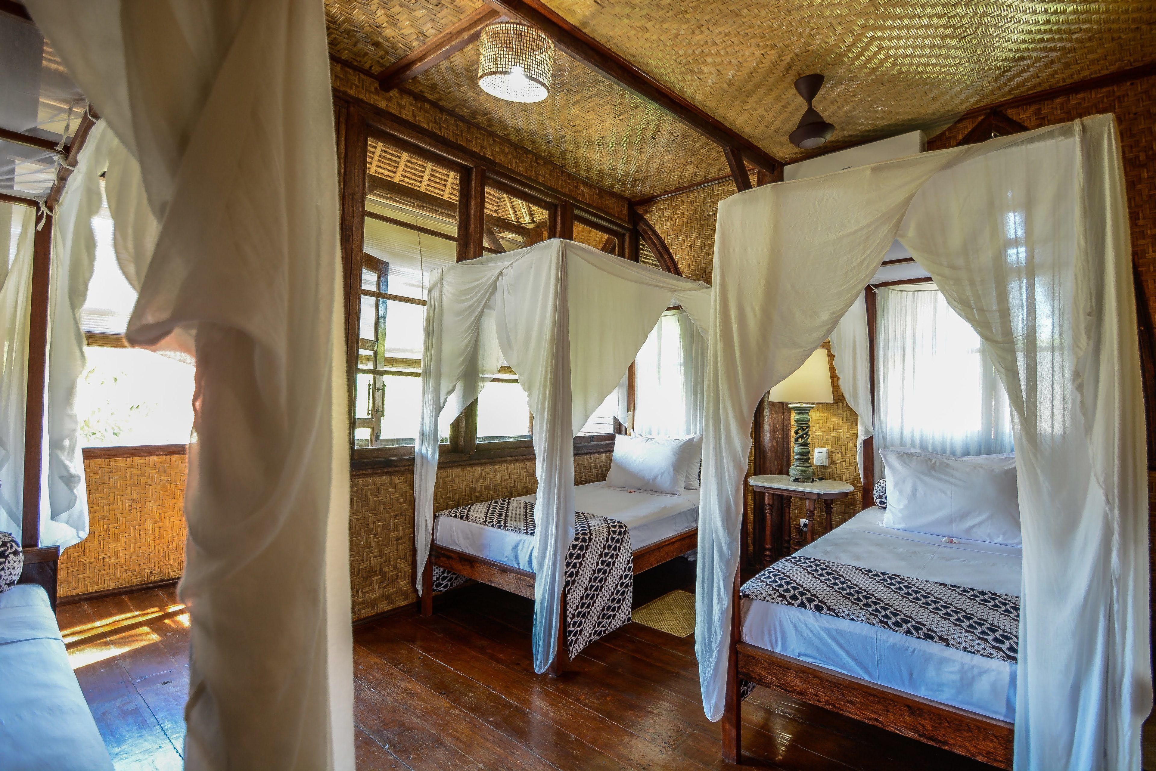 A room with two beds, each with a canopy, wooden floors, and a woven ceiling.