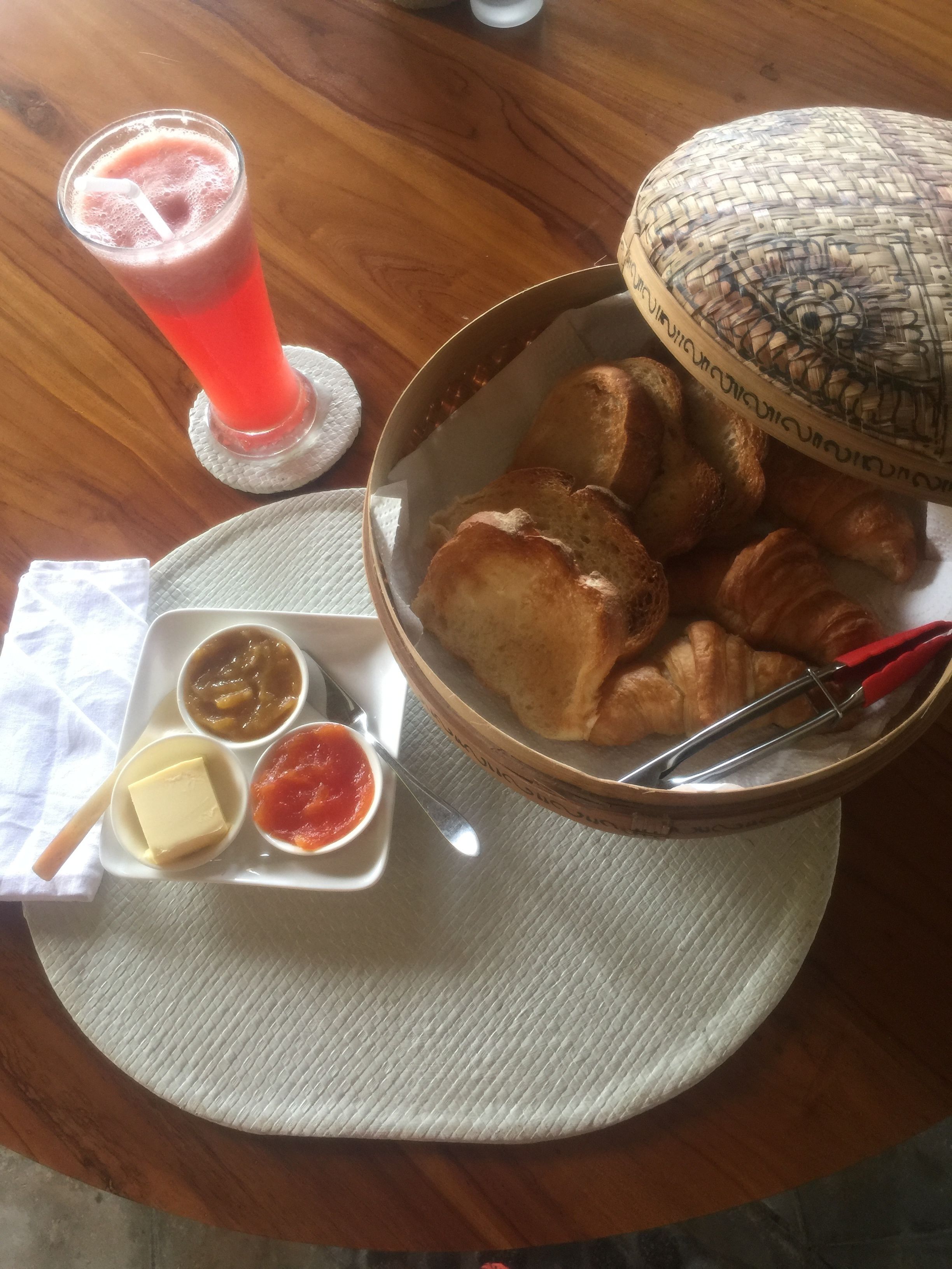 Uma mesa com uma cesta de pão, um copo de bebida vermelha e um prato com manteiga e acompanhamentos.