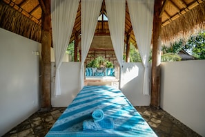 A room with a thatched roof, white curtains, a blue patterned bedspread, and a view of a garden. - Aashaya Jasri Resort (Karangasem)