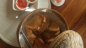 A table with a basket of bread rolls, a woven basket, a glass of red drink, and a plate with butter, chutney, and a sauce.