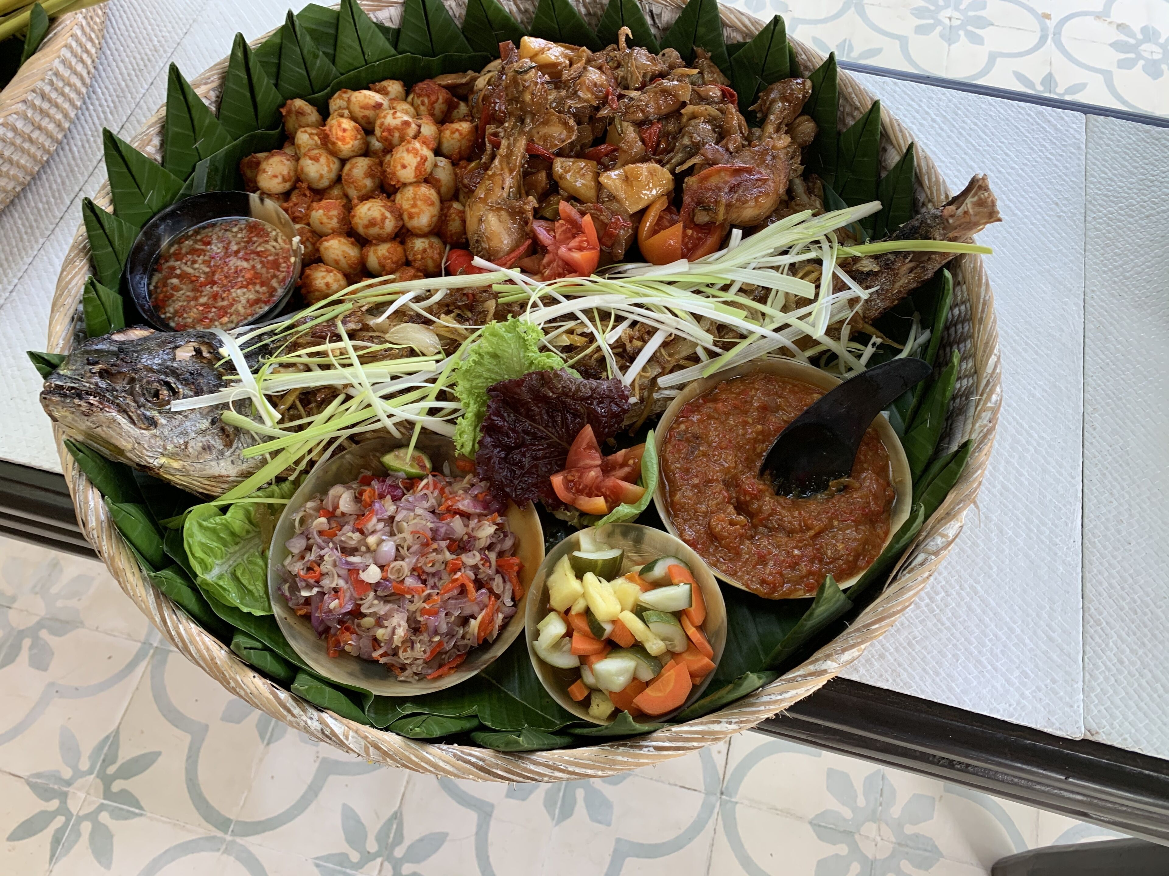 Un plato tradicional servido en una cesta tejida, con pescado, verduras y salsas variadas.