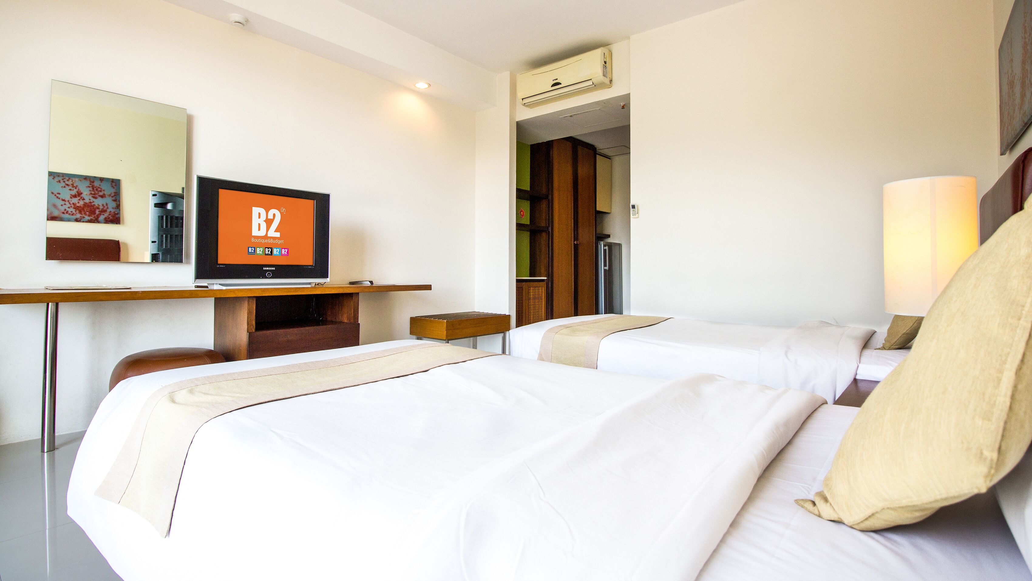 Een hotelkamer met twee bedden, een bureau met een televisie, een spiegel en een airconditioning.