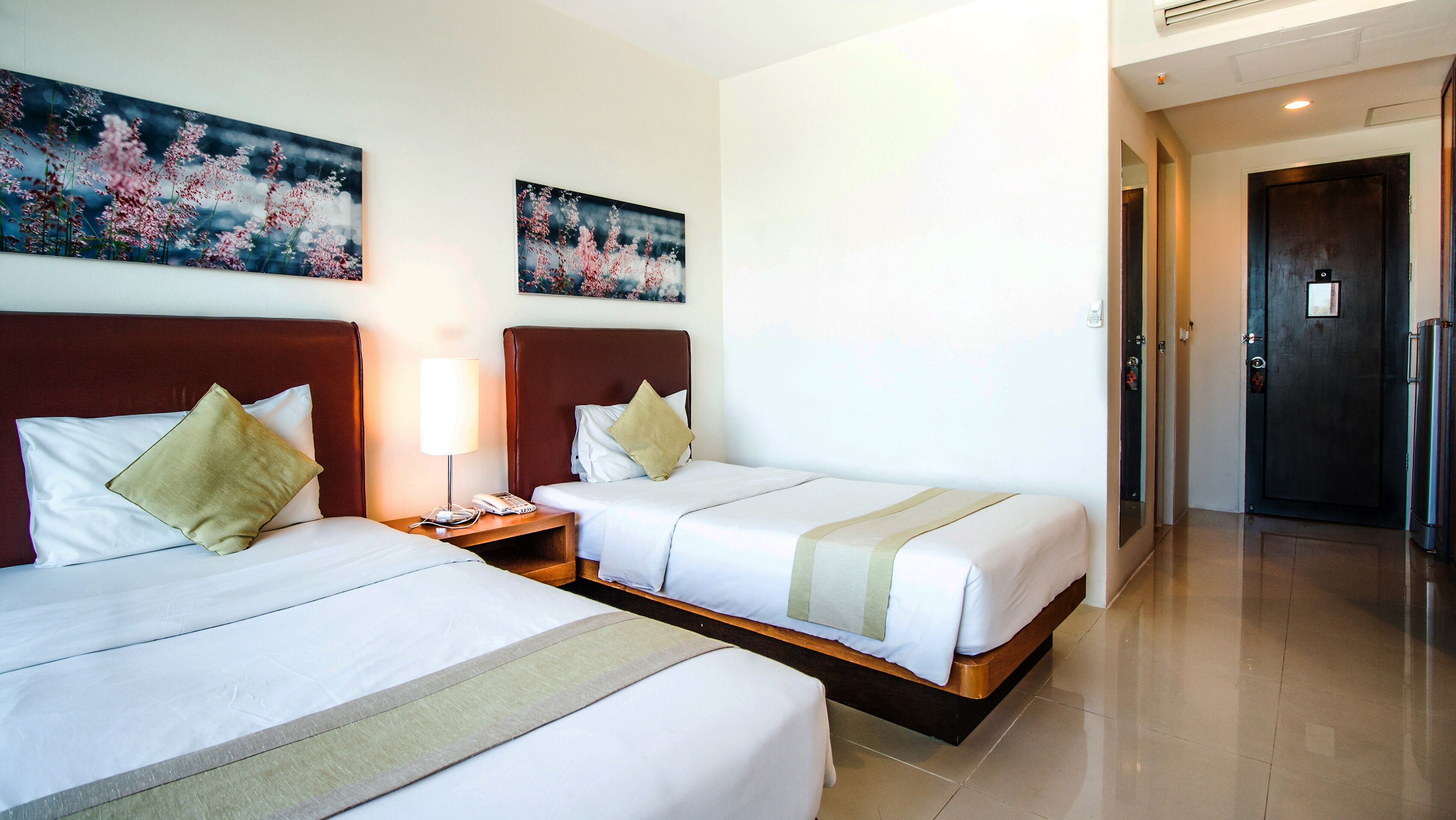 A hotel room with two beds, a nightstand with a lamp, and artwork on the walls.