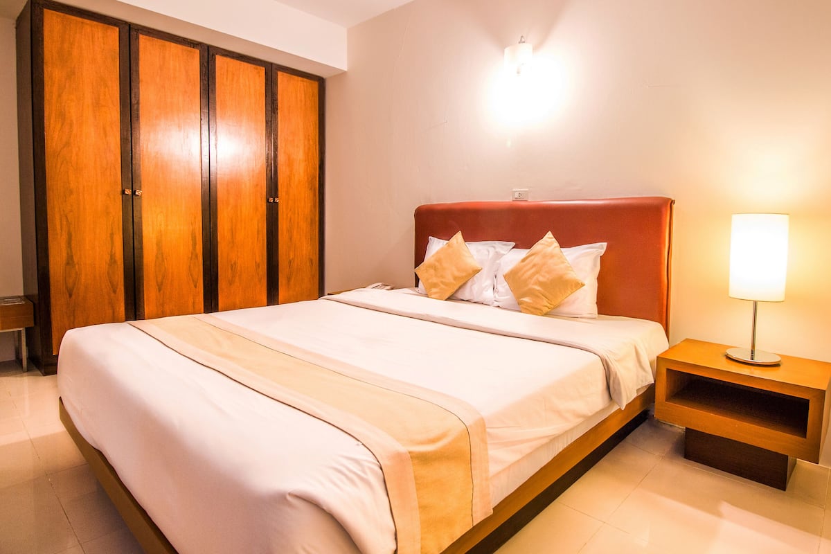 A neatly made bed with a headboard, a bedside table with a lamp, and a wardrobe.