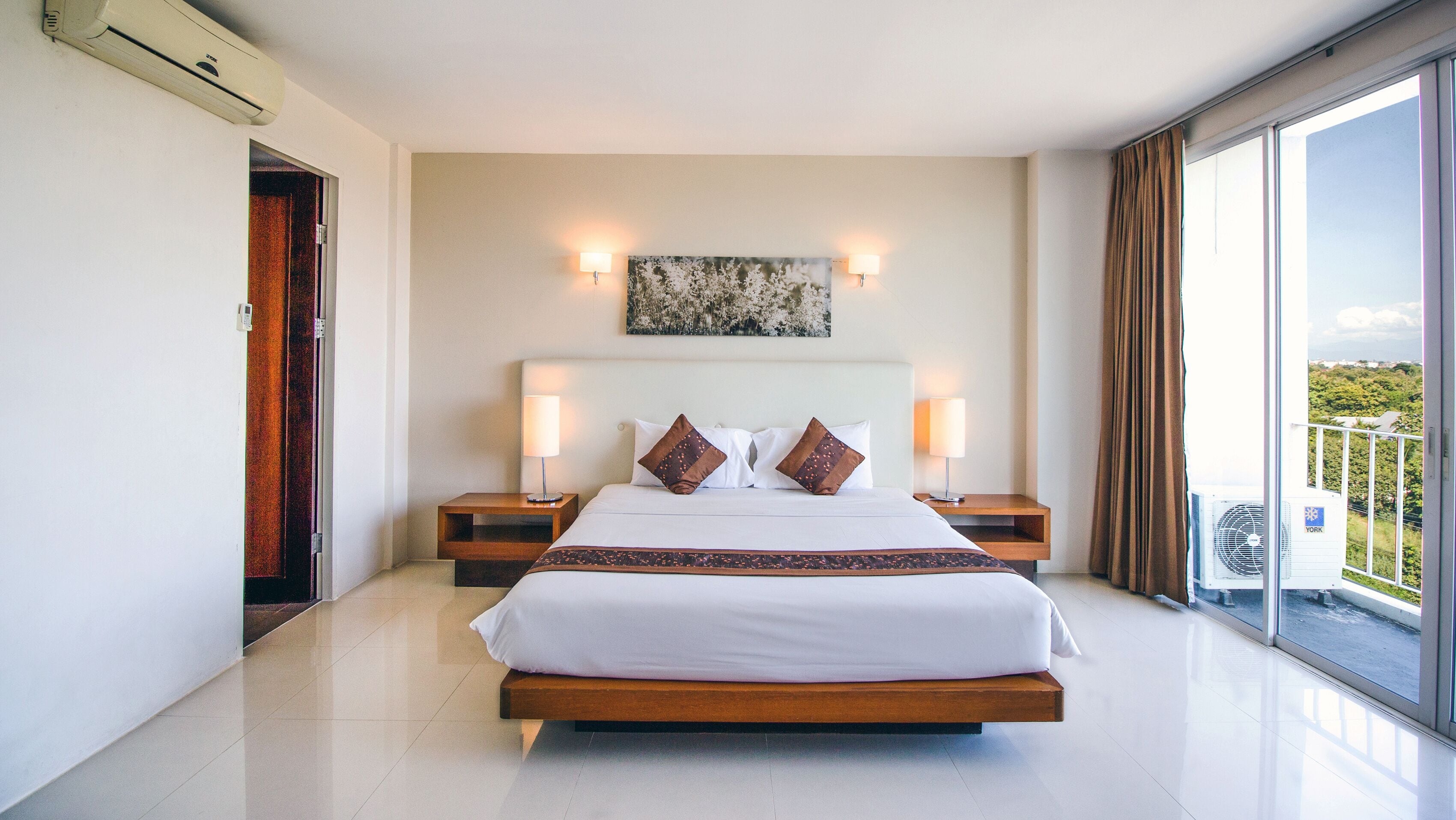 A modern hotel room with a large bed, two bedside tables with lamps, a ceiling fan, and a large window offering a view of the outdoors.